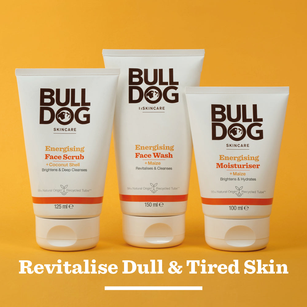 Three Bulldog Skincare products—Energising Face Scrub, Energising Face Wash, and Moisturiser—stand side by side on an orange background beneath the words “Revitalise Tired Skin.” All are crafted with natural origin ingredients.