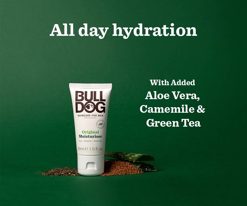 A tube of Travel Original Moisturiser stands on a green background with text: All day hydration and With added Aloe Vera, Camomile & Green Tea. Natural ingredients are scattered at the base of the tube.