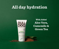 A tube of Travel Original Moisturiser stands on a green background with text: All day hydration and With added Aloe Vera, Camomile & Green Tea. Natural ingredients are scattered at the base of the tube.